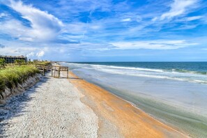 Une plage avec une promenade en bois menant à un bâtiment doté d’un toit plat.