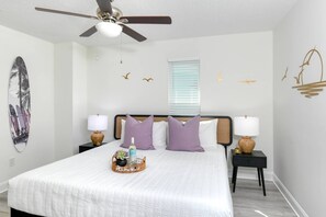 Une chambre à coucher comprenant un lit, deux tables de chevet, un ventilateur de plafond et des éléments de décoration murale.