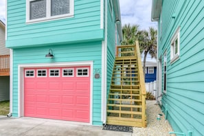 A turquoise two-story house with a red garage door, a wooden staircase, and a small porch area. - Steps to Private Beach Access, Ocean Views, Game Room, Brand New Furnishings, $300 in Free Tickets! (St. Augustine)