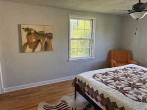 Ein Schlafzimmer mit einem Bett, einem Fenster, einem Gemälde und einem Sessel.