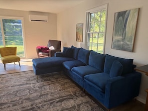 Ein Wohnzimmer mit einem Ecksofa, einem gelben Sessel, einem gemusterten Teppich und einem Gemälde an der Wand.