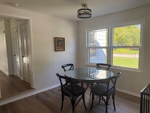 A dining area with a round glass table and four chairs, a ceiling light fixture, and a window with a view of a green landscape. - Fabulous 3-bedroom house with AC in welcoming Ames (Ames)