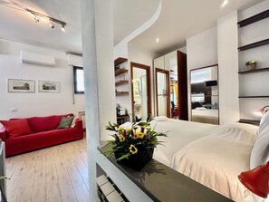Et moderne hotelværelse med seng, en rød sofa, et lille bord med blomster i en vase, og et badeværelse, der kan ses gennem en åben dør.