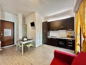 A compact kitchen with a dining table and chairs, a built-in oven, and a flat-screen TV mounted on the wall. - Perosi: A Modern Loft in Florence's Novoli Neighborhood (Firenze)