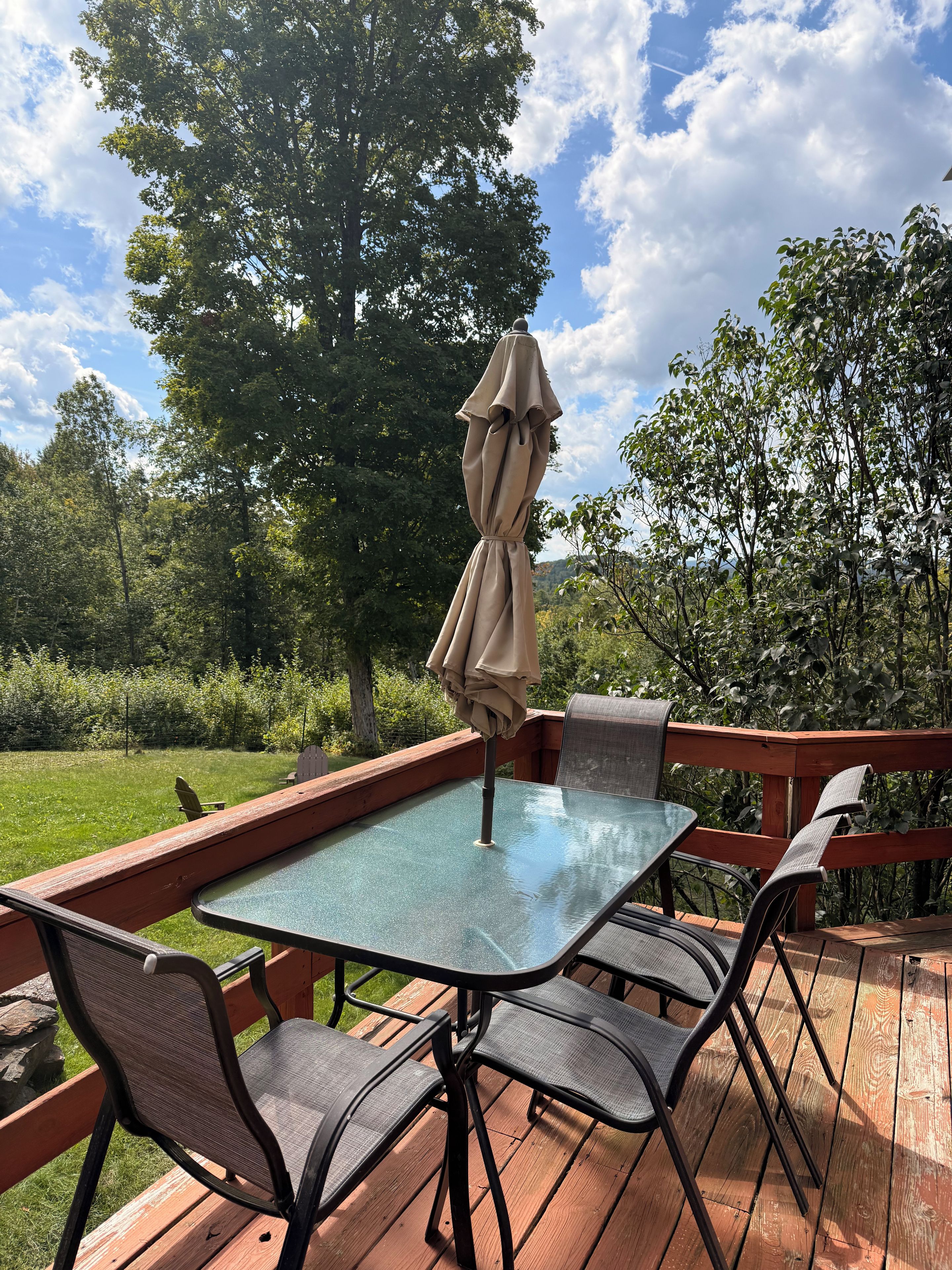 A glass-top table with four chairs and a single umbrella on a wooden deck.