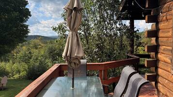 A wooden deck with a glass table and chairs, an umbrella, and a view of the surrounding greenery.