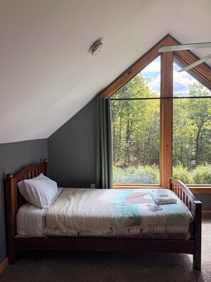 A single bed with a headboard, a window with curtains, and a ceiling vent.
