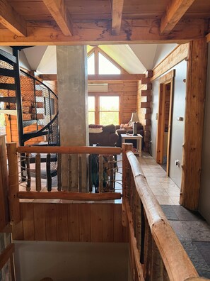 A wooden interior with a spiral staircase, a living area with a sofa and lamp, and a view through a window.