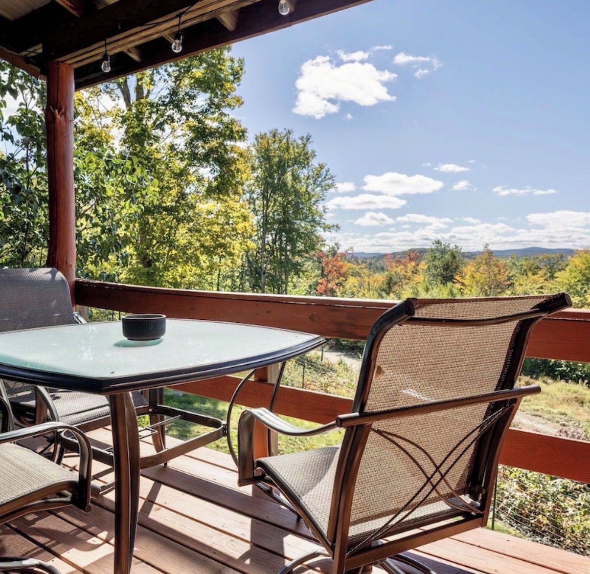 Een terras buiten met een tafel en stoelen, met uitzicht op een bebost landschap.