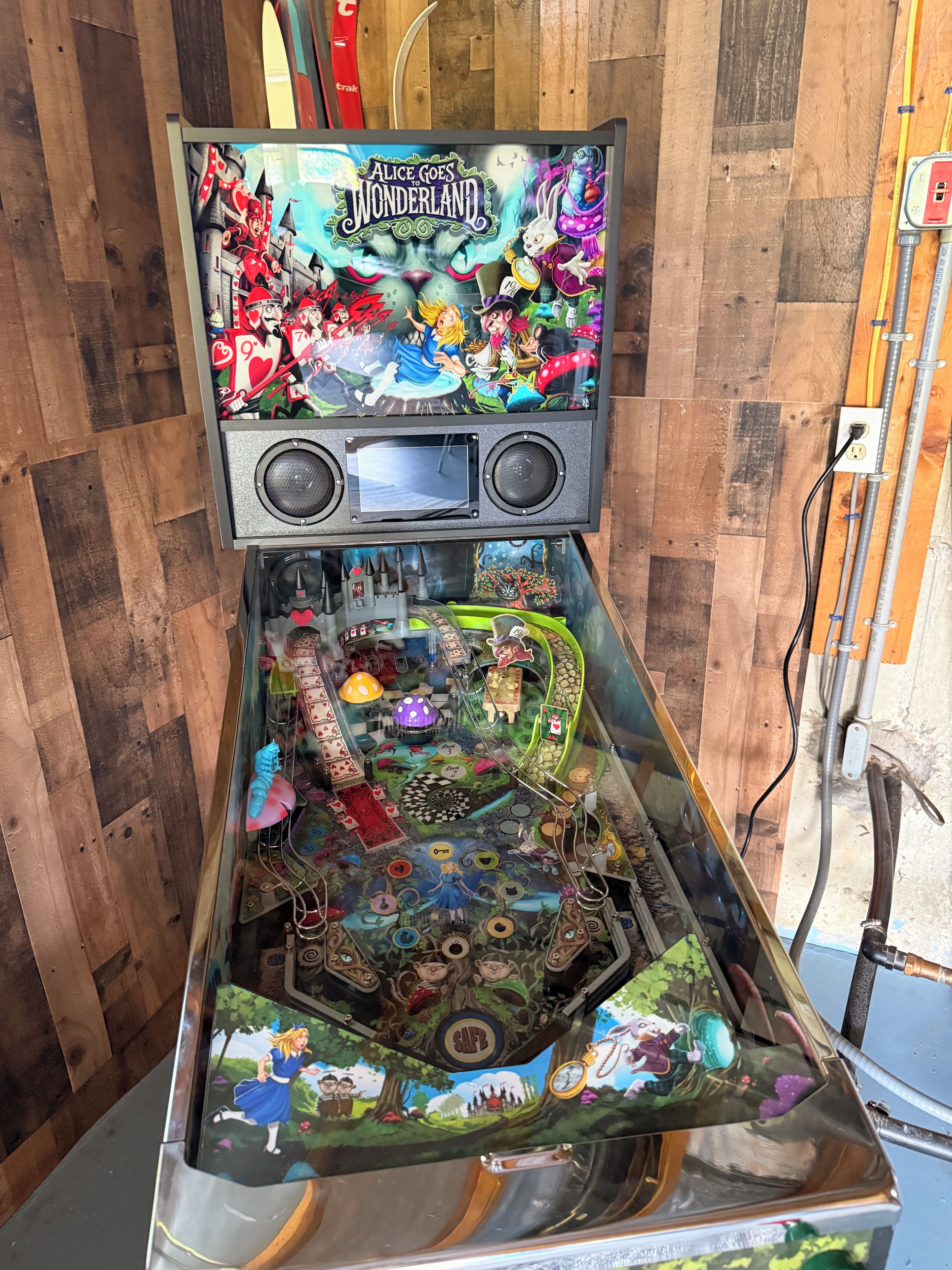 Una máquina de pinball con temática de Wonderland, que presenta una pantalla grande en la parte superior y varios elementos de juego debajo.