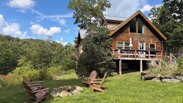 A cabin with a deck, a fire pit, and Adirondack chairs.