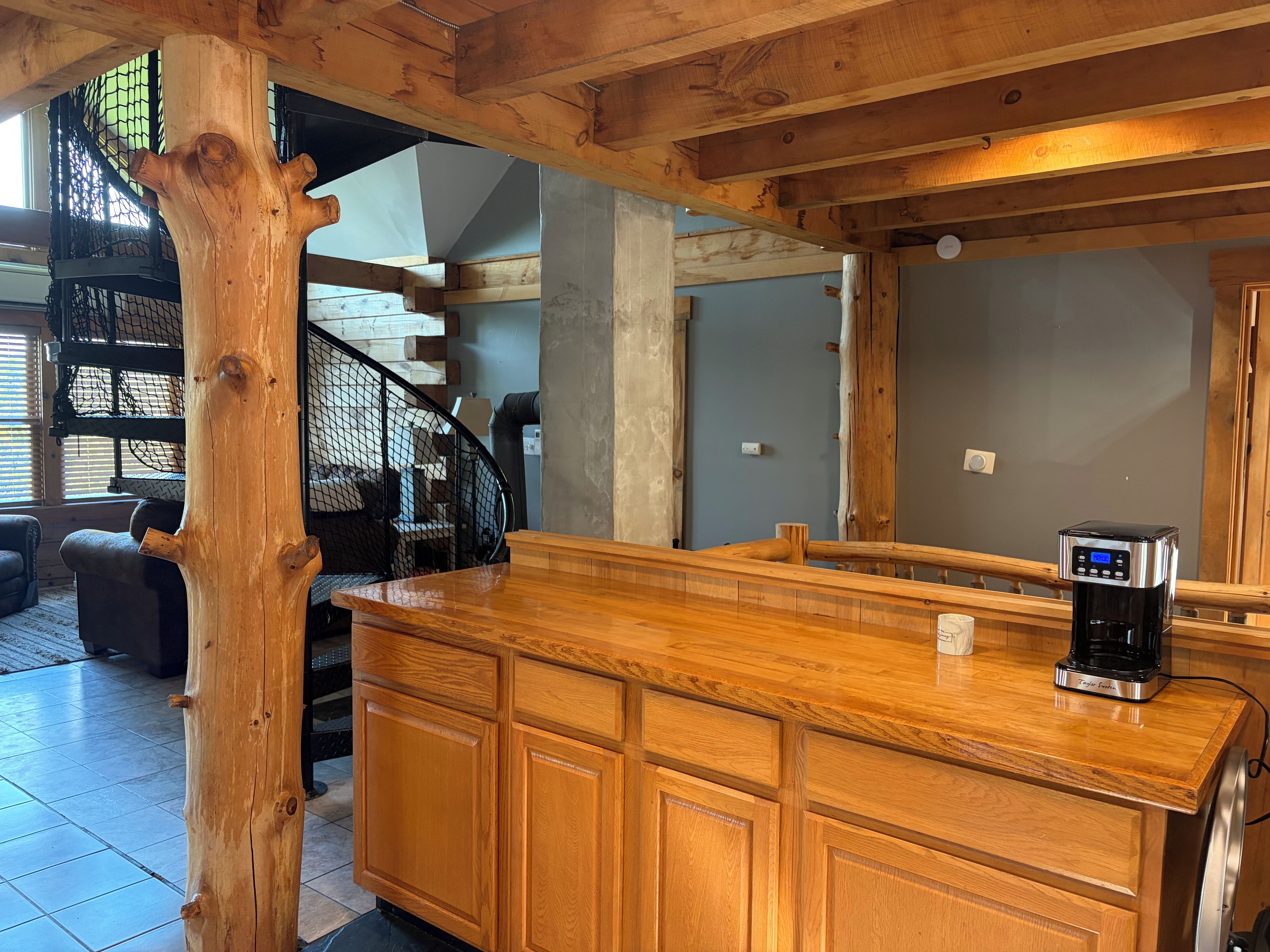 Un'isola cucina in legno con una macchina per il caffè, una scala con ringhiera in rete e vista su un soggiorno con un divano.
