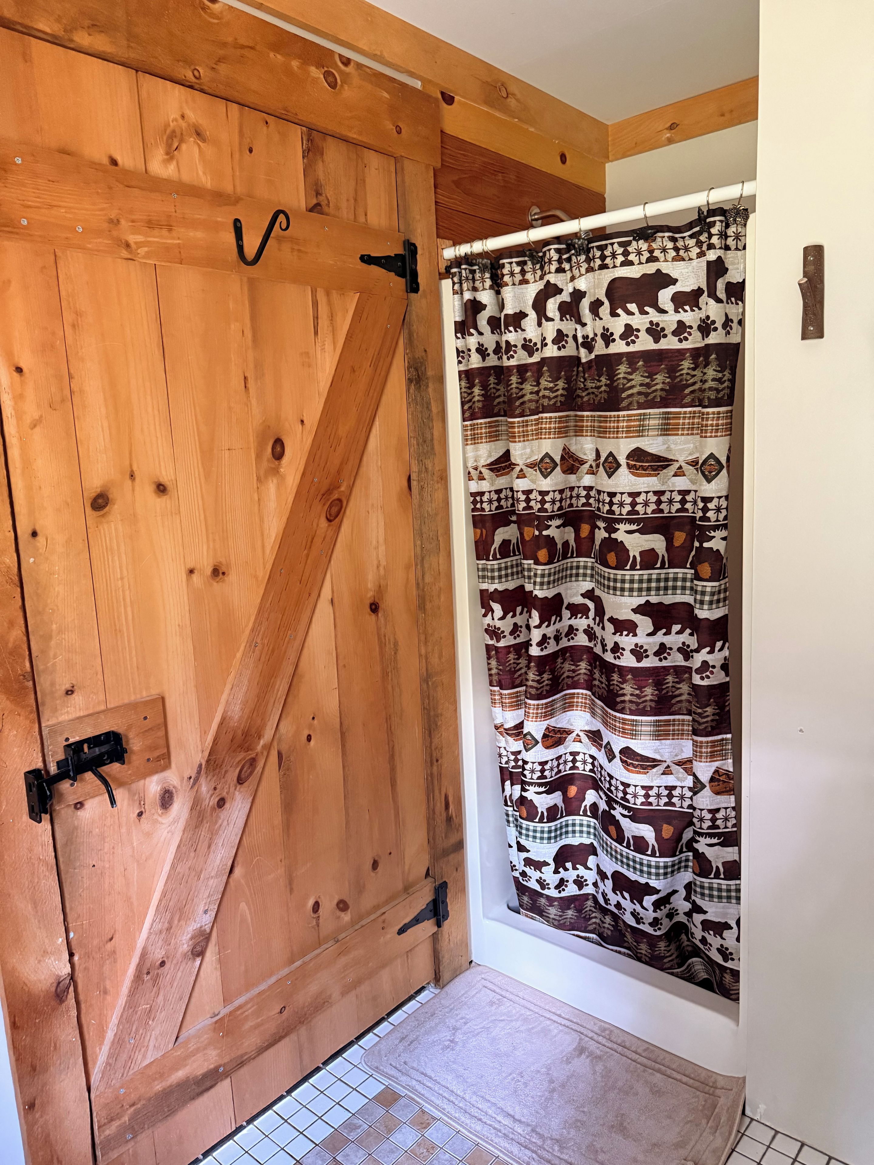 Une porte en bois avec un loquet noir, un rideau à motifs et un sol carrelé.