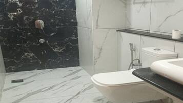 A bathroom with a marble floor, a white toilet, a glass shower enclosure, and a towel rack.