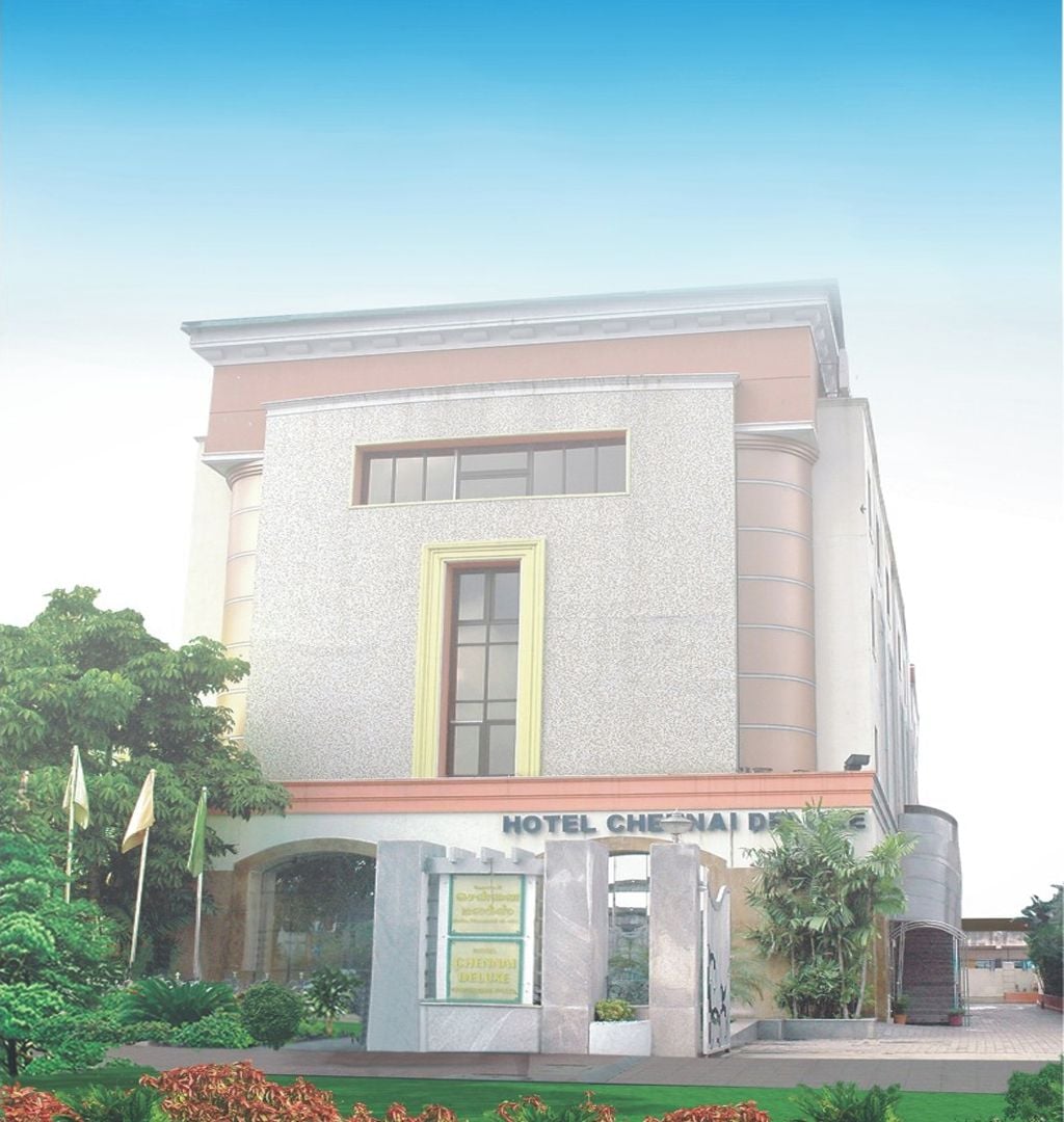 A hotel with a prominent entrance, a signboard, and a well-maintained garden.