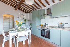 A kitchen with white cabinets, a stove, and a sink. There is a clock on the wall and a dining table with chairs. - A charming 67 sqm apartment with a view of the Baptistery of San Giovanni, ideal for four people. The apartment, located on the second floor of a building (NO elevator; apartment not suitable for people with disabilities: several internal steps), is situ (Pisa)