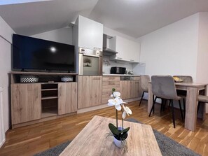 A modern kitchen with white cabinets, a flat-screen TV, and a dining area with a table and chairs.