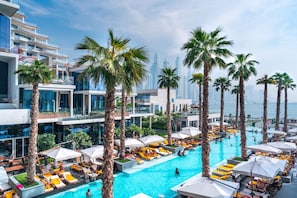 A rooftop pool area with palm trees, sun loungers, and a view of the city skyline. - Modern 2BR Gem Prime Palm Jumeirah Location (Dubai)