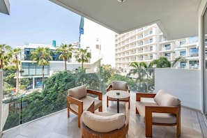 A balcony with a seating area, including two sofas and a small table, overlooking a cityscape with modern buildings and palm trees. - Modern 2BR Gem Prime Palm Jumeirah Location (Dubai)