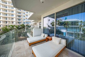 A modern hotel room with a glass balcony, two white sofas, and a view of a high-rise building and palm trees. - Modern 2BR Gem Prime Palm Jumeirah Location (Dubai)