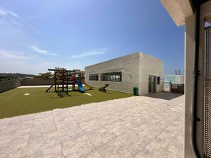 Eine Dachterrasse mit künstlichem Rasen, einer Spielanlage und einem modernen Gebäude.