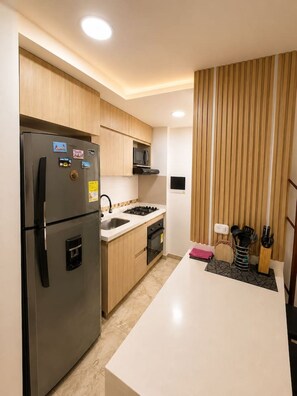 Eine moderne Küche mit einem Edelstahlkühlschrank, einer Mikrowelle, einem Gasherd und Holzschränken.