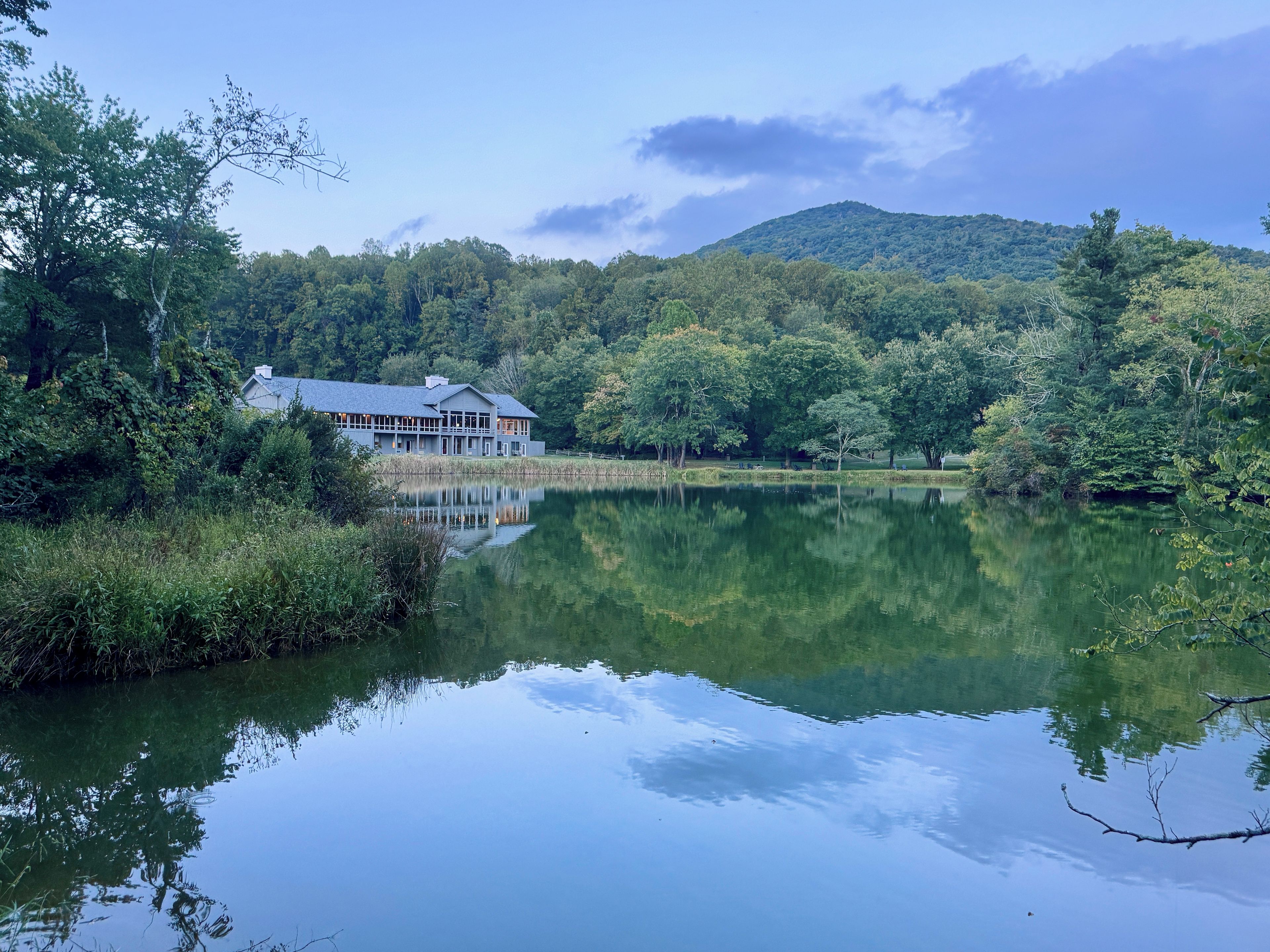 Une propriété au bord d’un lac, avec une grande maison, entourée d’une forêt dense et d’une montagne en arrière-plan.