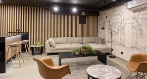 Ein modernes Interieur mit einer Couch, einem Couchtisch und Sesseln, einem Schreibtisch mit Computer sowie einer Wand mit architektonischen Skizzen.