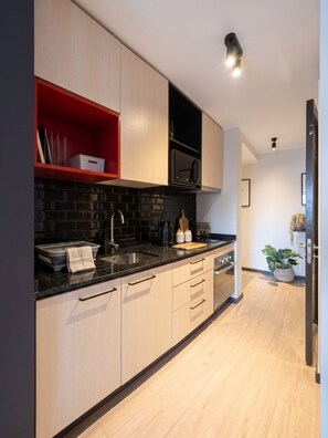 A modern kitchen with light wood cabinets, a black countertop, and a red shelf. - Edificio Santiago Tres by Domus Travels (Santiago)
