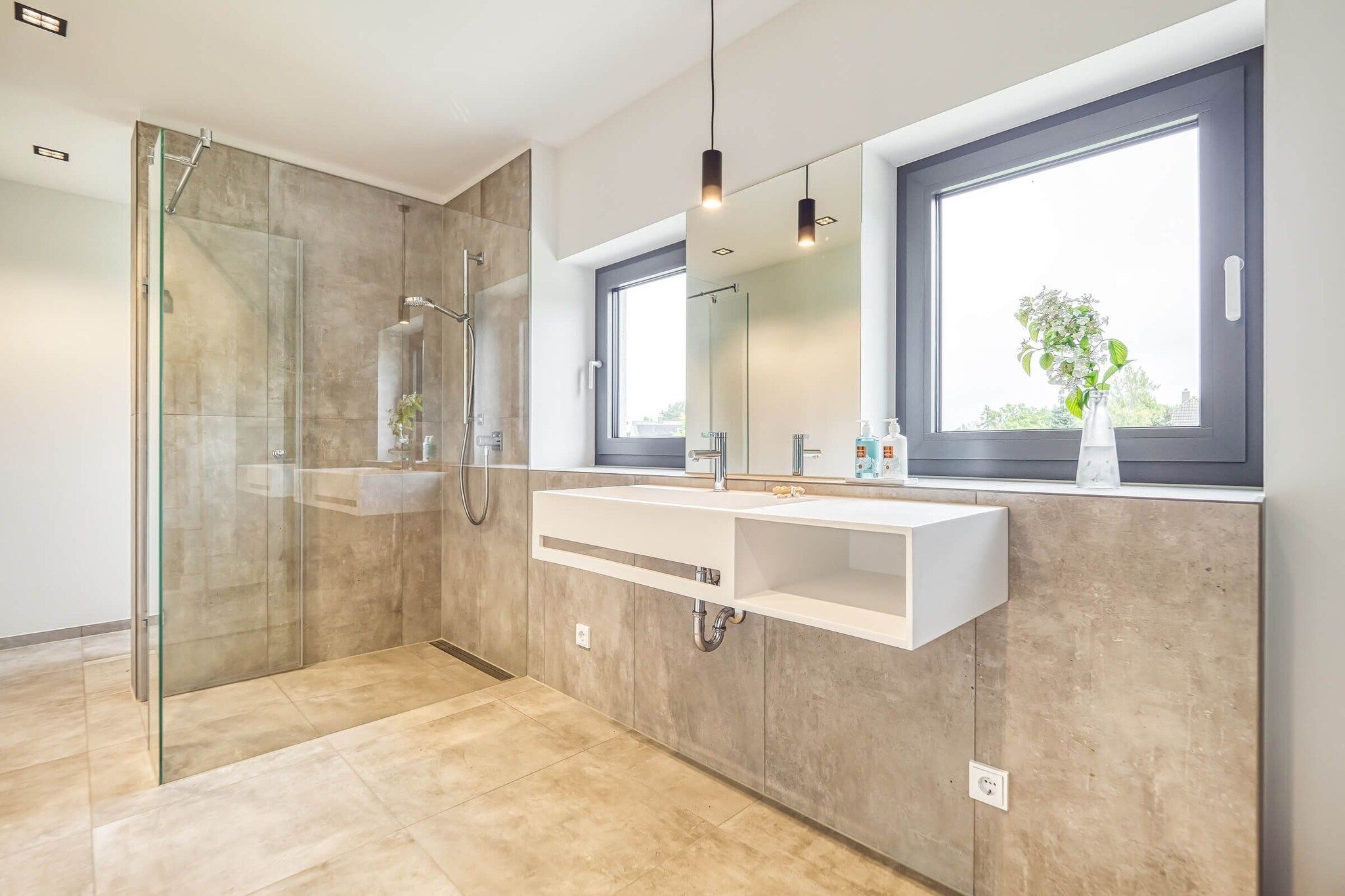 A modern bathroom with a glass-enclosed shower, a large mirror, and a window providing natural light.