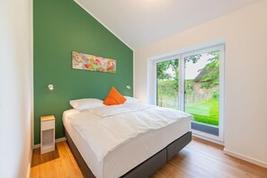 Ein Schlafzimmer mit einem Bett, einem Nachttisch, einer grünen Wand und einem Fenster mit Blick auf einen Garten.