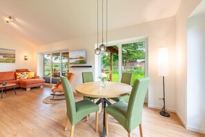 Ein modernes Wohnzimmer mit einem runden Esstisch, grünen Stühlen, einer Couch und einem an der Wand befestigten Fernseher.