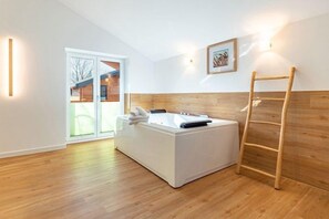 A modern bathroom with a bathtub, a wooden ladder, and a sliding glass door leading to an outdoor area. - Ferienhaus mit Sauna und Whirlpool in Kating (Tönning OT Kating)