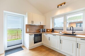 A modern kitchen with white cabinets, a wooden countertop, and a view of a vineyard through a sliding door. - Ferienhaus mit Terrasse und Sauna in Kating (Tönning OT Kating)