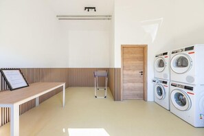 A laundry room with a bench, a drying rack, and stacked washing machines. - Ferienhaus mit Terrasse und Sauna in Kating (Tönning OT Kating)