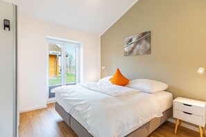 A bedroom with a bed, a nightstand, a window, and a door. - Ferienhaus mit Terrasse und Sauna in Kating (Tönning OT Kating)