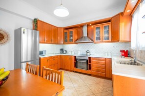 Cozinha compacta com armários de madeira, geladeira de aço inoxidável, forno embutido e pia com torneira moderna.