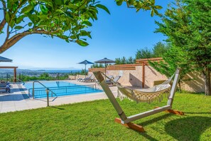 Área de piscina com espreguiçadeiras e guarda-sóis, uma rede e vista para a paisagem.