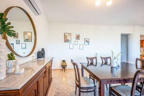 Uma área de refeições com bancada de mármore, cadeiras de madeira, mesa redonda e obras de arte na parede.