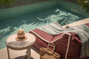 Ein Pool-Loungebereich mit Liegestuhl, einem kleinen Tisch mit einem Getränk und einem gewebten Korb.