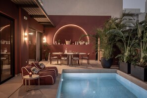 Un área de piscina moderna al aire libre con sillas de descanso, una mesa de comedor y diversas plantas.