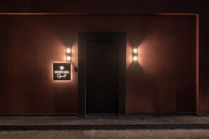 Ein Hotel Eingang mit einer dunklen Tür, zwei Wandleuchten und einem Schild darüber.