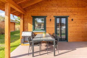 Eine Holzblockhütte mit überdachter Terrasse, einem Esstisch mit Stühlen und einer Schiebetür.