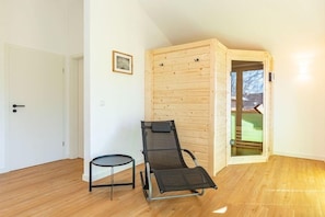 A room with a wooden wall, a black chair, a small round table, and a door. - Familienferienhaus mit Sauna und Whirlpool (Tönning OT Kating)