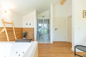 Ein modernes Zimmer mit Holzboden, einer weißen Wand mit Holzakzent, einer Glastür, die auf einen Balkon führt, und einem kleinen Tisch mit einer Pflanze.
