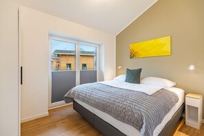 A bedroom with a bed, a nightstand, a window, and a view of buildings outside. - Ferienhaus mit eigener Sauna und schoener Terrasse (Tönning OT Kating)