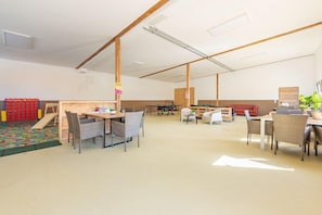 A spacious indoor area with tables and chairs, a play area with a slide, and a wooden bench. - Ferienhaus mit eigener Sauna und schoener Terrasse (Tönning OT Kating)