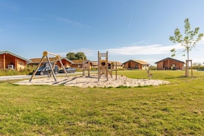 A campground with wooden cabins, a swing set, and a clear sky. - Ferienhaus mit eigener Sauna und schoener Terrasse (Tönning OT Kating)