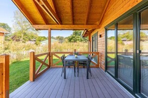 A wooden deck with a table and chairs, surrounded by glass doors and windows. - Ferienhaus mit eigener Sauna und schoener Terrasse (Tönning OT Kating)