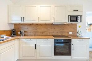 A modern kitchen with white cabinets, a wooden countertop, a built-in microwave, a coffee maker, and a stove. - Ferienhaus mit eigener Sauna und schoener Terrasse (Tönning OT Kating)